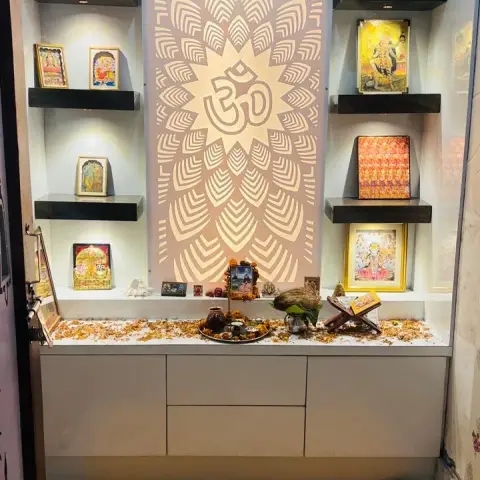 A backlit CNC-cut Om jaali panel forms the focal wall of this pooja unit, flanked by floating shelves for framed deities above a closed storage counter.