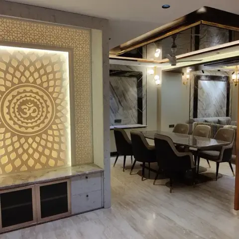 A backlit Om mandala panel set into a marble-clad pooja niche with a drawer base, looking across the dining table to a floor-to-ceiling laser-cut wooden jaali