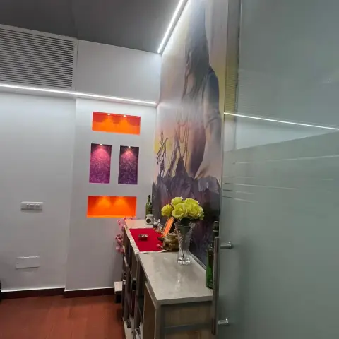 A backlit pooja corner in a hallway with a large printed mural of a deity, LED-lit orange and purple wall niches