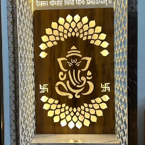 A backlit pooja unit with a CNC-cut Ganesha motif panel, jaali side panels, and a marble-finish storage base.