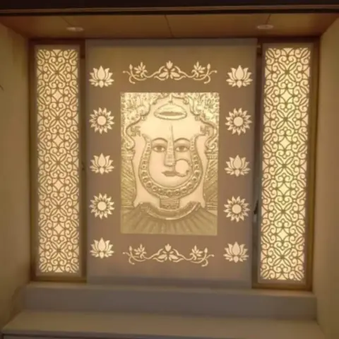 A backlit pooja wall featuring an engraved deity motif panel flanked by jaali-cut side screens, above a floating cabinet with drawer storage.
