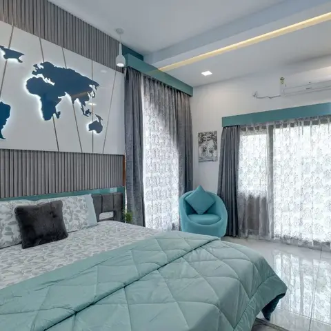 A backlit world-map wall panel above a fluted grey headboard wall, with a teal accent chair and a study desk in the corner.