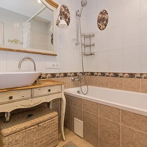 A bathroom with a vintage wood vanity holding a countertop basin next to a tiled tub with floral accent tiles.