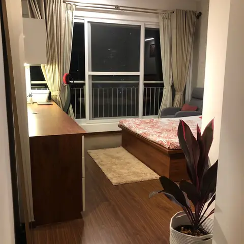 A bedroom at night with a built-in wood study desk along one wall, a wood-framed bed with floral-print bedding, a beige shag rug