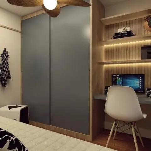 A bedroom corner with a grey sliding-door wardrobe framed in wood, and an adjoining built-in study nook with backlit open shelving above a wall-mounted desk.