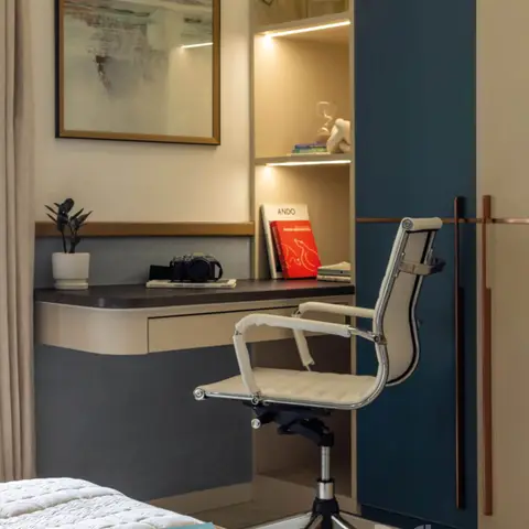 A bedroom study nook with a floating two-tone desk, backlit display shelving styled with books and a camera, and a teal wardrobe panel beside it.