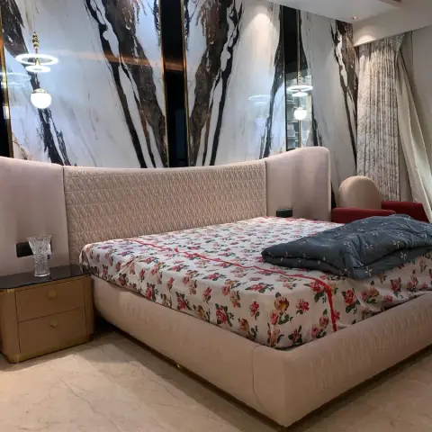 A bedroom with a book-matched marble and brass feature wall behind an upholstered wingback bed and gold-trimmed nightstands.