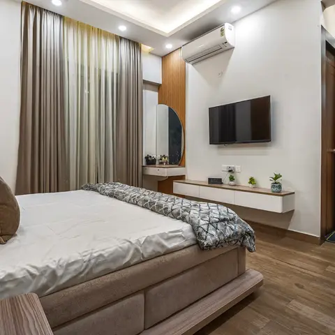 A bedroom with a cove-lit ceiling shows a floating TV console beside a round vanity mirror nook and a wood-slat headboard wall, opening onto a hallway.
