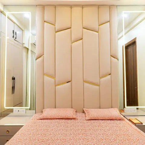 A bedroom with a cream channel-tufted headboard wall accented by gold trim strips, flanked by two tall backlit LED-framed mirrors