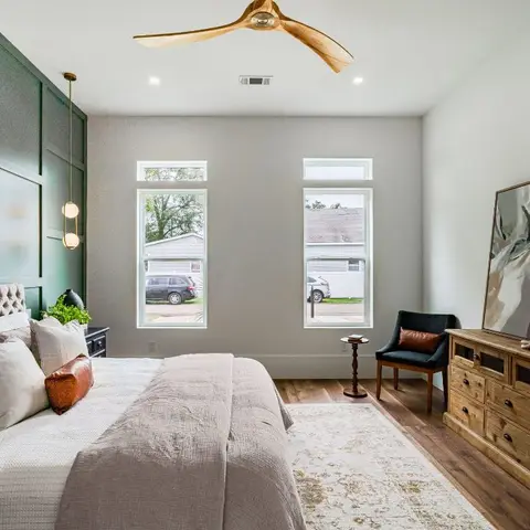 A bedroom with a deep green grid-paneled accent wall behind a tufted grey headboard, a wood dresser doubling as a TV console