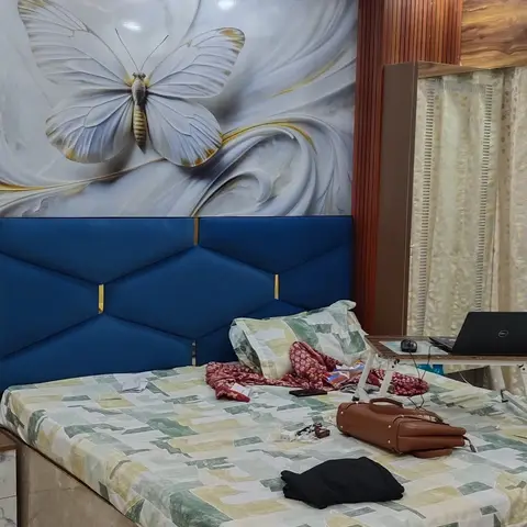 A bedroom with a diamond-tufted royal-blue headboard beneath a marble-and-butterfly wallpaper mural, a fluted wood ceiling-height accent column