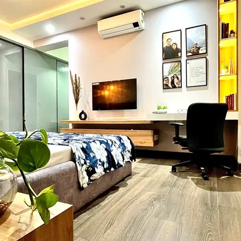 A bedroom with a floating wood TV console, a built-in study nook lit by a backlit open display shelf, and a gallery wall of framed family photos above the desk.