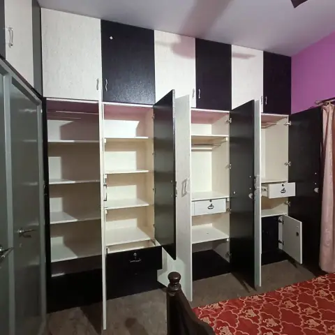 A bedroom with a floor-to-ceiling black-and-white wardrobe wall shown fully open, a magenta accent wall, and a red medallion-print bedsheet.