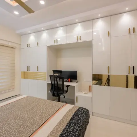 A bedroom with a full-wall white gloss wardrobe featuring a built-in study niche and gold mirror-strip accents.