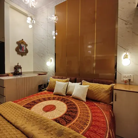 A bedroom with a glossy gold channel-panelled headboard wall, marble side walls, bead-drop wall sconces, and a red mandala-patterned bedspread.