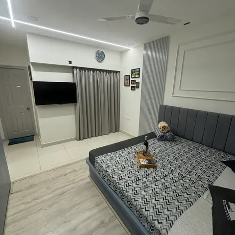 A bedroom with a grey channel-tufted headboard, a chevron-patterned bedspread, and a wall of framed family photos beside a fluted grey panel.
