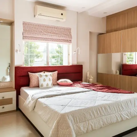 A bedroom with a maroon upholstered headboard, a mirrored wood-finish sliding wardrobe, and a patterned roman blind over the window.