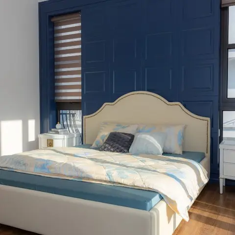 A bedroom with a navy blue raised-panel wall behind a cream nailhead-trim upholstered bed and matching brass-accented nightstands.