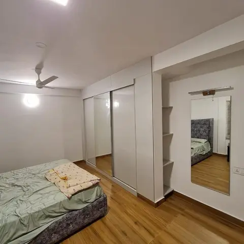 A bedroom with a white high-gloss sliding-door wardrobe, a grey upholstered bed base with a plain green cover