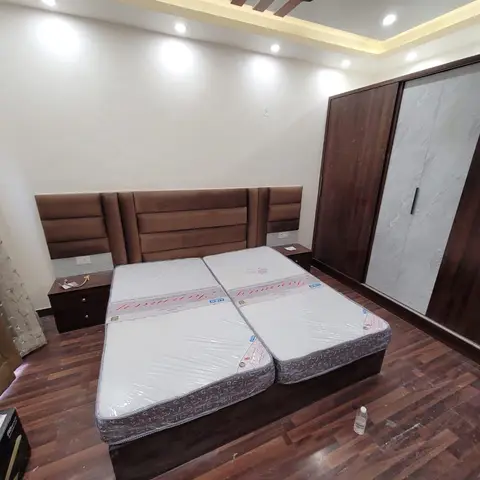 A bedroom with a wide brown channel-tufted headboard, a dark wood wardrobe with marble-effect sliding doors