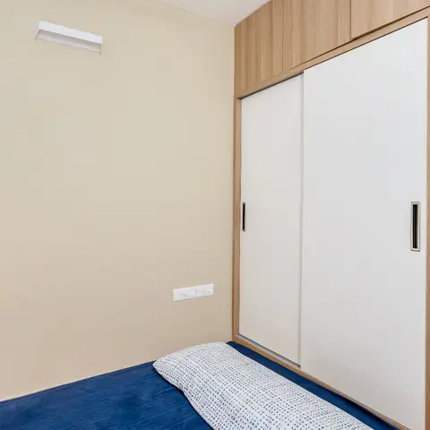 A bedroom with a wood-and-white sliding-door wardrobe wall and a navy bedspread, lit by a single wall sconce.