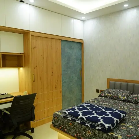 A bedroom with a wood-tone sliding wardrobe with a teal accent panel, a built-in study desk