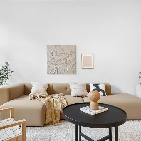 A beige curved-arm sectional sofa with a black round coffee table, a textured abstract canvas and framed print on the wall
