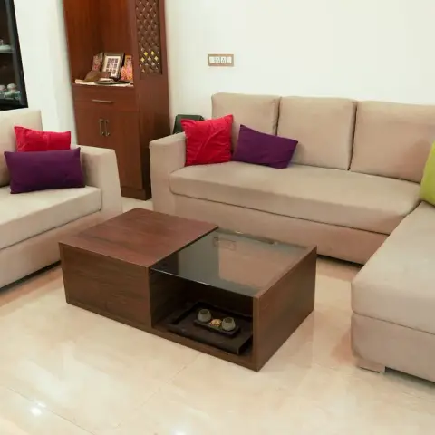 A beige fabric L-sectional and matching two-seater around a walnut coffee table with an inset glass top, scattered with red, purple, lime and blue cushions