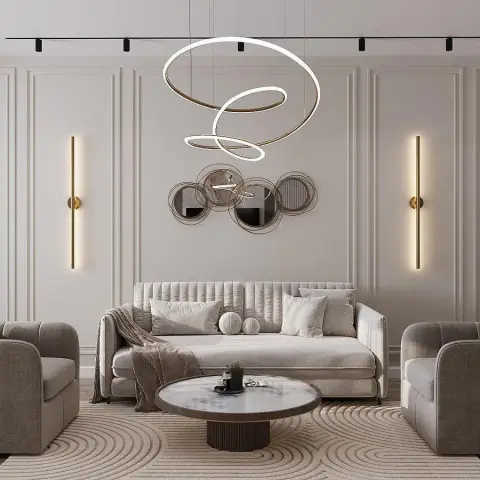 A beige living room with fully panelled walls, a sculptural gold ring pendant chandelier, a cluster of round mirrors