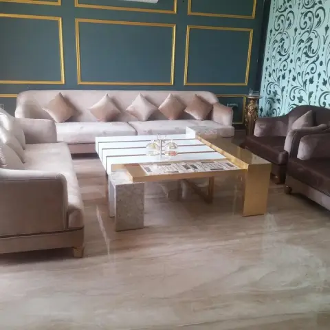 A beige velvet L-shaped sofa and mauve armchairs around a mixed marble-and-brass coffee table