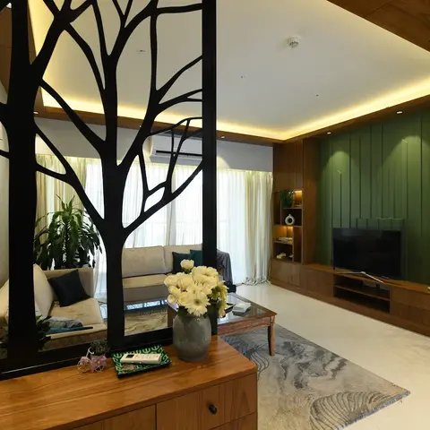 A black laser-cut tree-branch screen divides the entry from a living room with a forest-green fluted TV accent wall, walnut console cabinetry