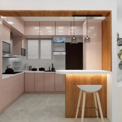 A blush-pink handleless modular kitchen in an L with a wood-clad breakfast counter closing the fourth side, a white herringbone mosaic dado