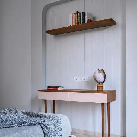 A blush-pink kids' bedroom nook with a curved wall-panelled niche, a floating wood bookshelf