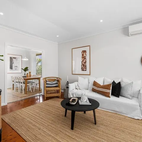 A boho living room with a white slipcovered sofa styled with rust and black cushions, a round leather-strap mirror, a black round coffee table