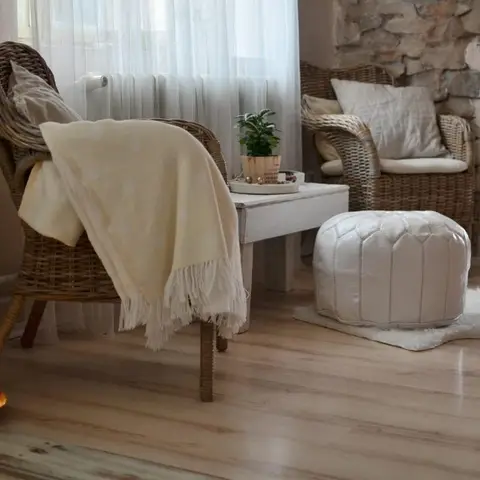 A boho reading nook with a wicker armchair draped in a cream throw, a tufted white pouf, and a faux-fur rug beside a stacked stone accent wall.
