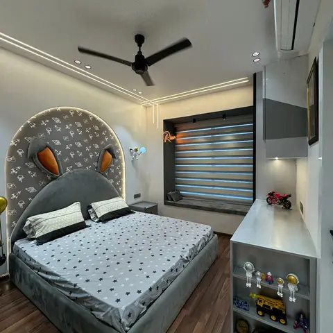 A boy's bedroom with a rocket-print arched headboard shaped like animal ears, star-print bedding, a neon name sign, window seat and an open toy display shelf