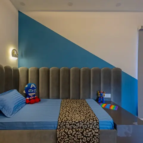 A boy's bedroom with a two-tone geometric blue and white painted wall behind a scalloped grey channel-tufted upholstered headboard