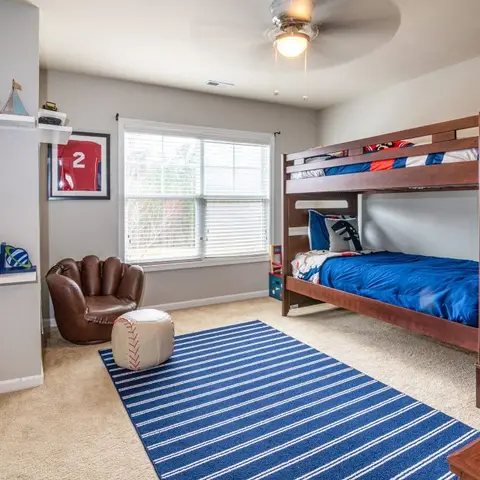 A boy's sports-themed bedroom with a built-in staircase bunk bed, a baseball-glove chair and a navy striped rug