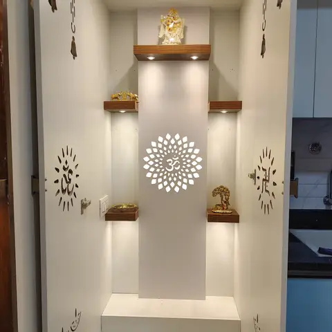 A built-in pooja cabinet with a backlit laser-cut Om jaali panel flanked by lit deity niches, and swastik-motif cutouts on the inner cabinet doors.