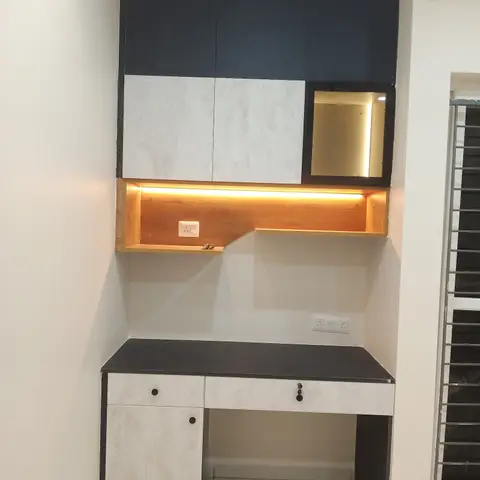 A built-in study desk niche with navy blue and marble-effect overhead cabinets, a backlit open shelf, and a black-top desk with storage drawers below.