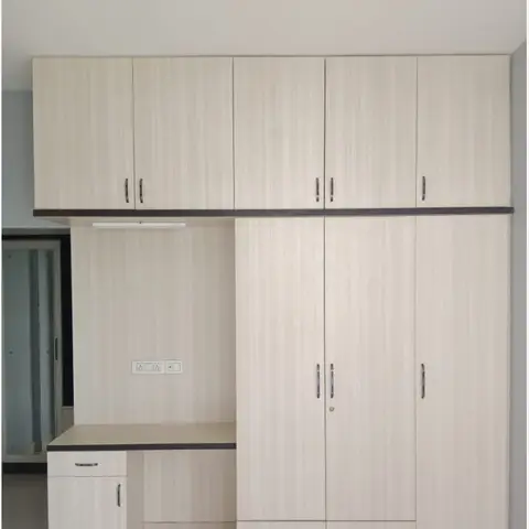 A built-in study desk with a drawer unit beside a floor-to-ceiling wardrobe with overhead loft cabinets, in light oak-finish laminate.