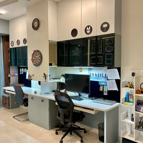 A built-in study desk with two workstations under glossy black-and-white overhead cabinets, personalized with Marvel-themed wall decals, a dartboard