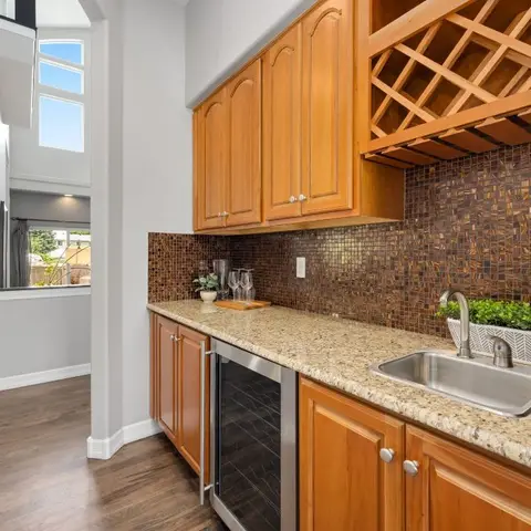 A butler's-pantry wet bar with a diamond-lattice wood wine rack, brown glass mosaic backsplash, granite counter, sink and built-in wine fridge.