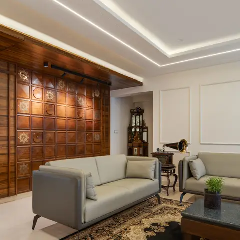A carved wood feature wall in a brass-inlaid grid pattern anchors a living room with grey leather sofas