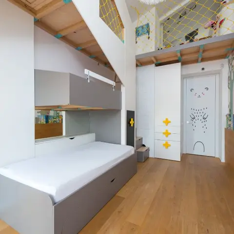 A child's bedroom with a grey storage bed under a mezzanine play loft with netting, a hand-painted bear-face door, and a whimsical forest-animal wall mural