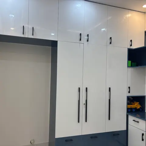 A child's room with a high-gloss white and slate-blue wardrobe wall, open toy shelves and a built-in study desk nook