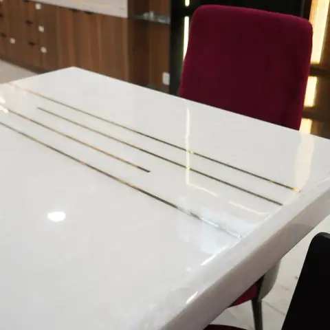 A close-up of a white marble dining table inlaid with thin brass lines, paired with maroon velvet chairs