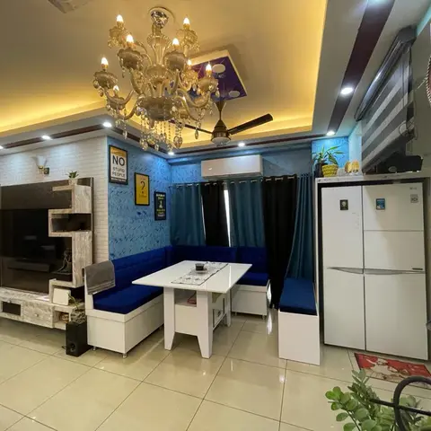 A cluttered open-plan corner with a blue booth dining nook, a TV console, and a refrigerator, styled with a crystal chandelier and quirky text-based wall art