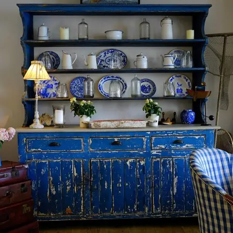A coastal-style dining corner with a distressed indigo-blue Welsh dresser displaying blue-and-white china, a brass lamp
