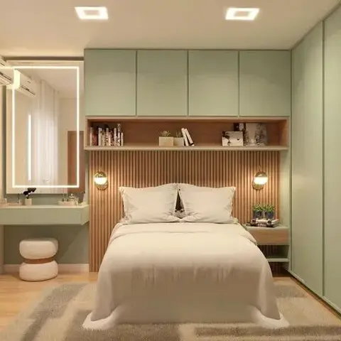 A compact bedroom with sage-green overhead wardrobes, a fluted-wood headboard wall lit by twin wall sconces